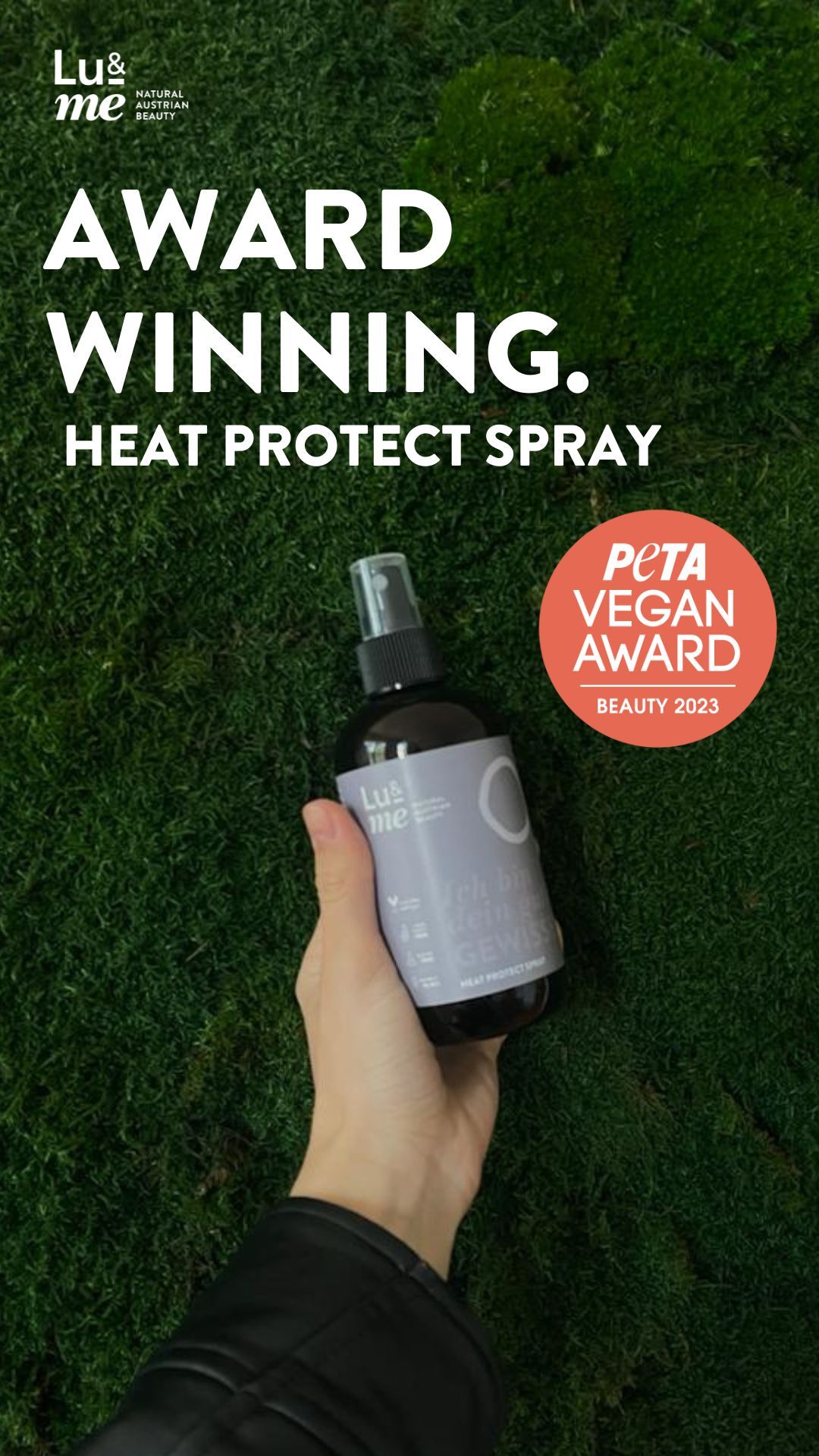Braune Sprühflasche in Hand. PETA Vegan Award. Text: Award Winning. Heat Protect Spray. Auf Moos Hintergrund.