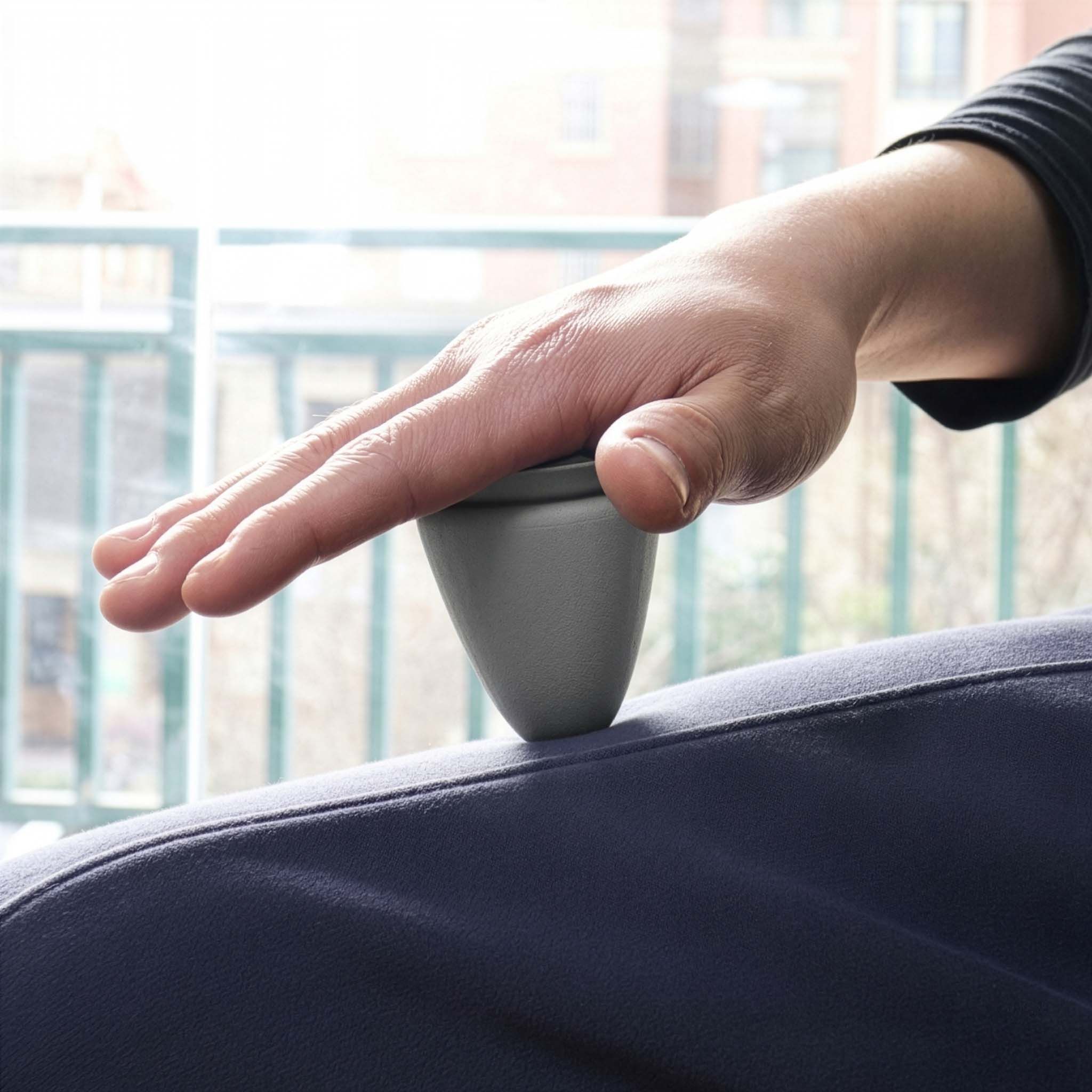 Graues, kegelförmiges Produkt wird auf dem Oberschenkel einer Person platziert. Hand auf dem Produkt.