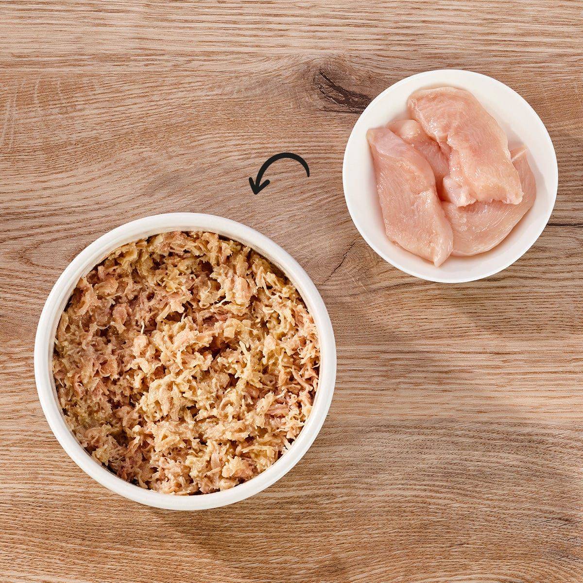 Zwei Schalen auf Holz. Eine mit zerkleinertem Futter, eine mit Hühnerfleisch. Pfeil zeigt von Futter zu Fleisch.