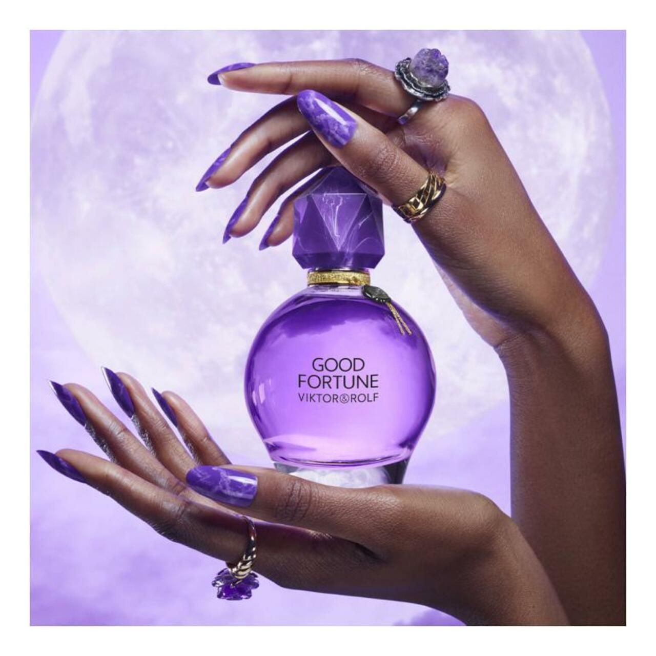 Hände halten Flakon. Aufschrift: GOOD FORTUNE VIKTOR & ROLF. Facettierter Deckel. Ringe an Fingern.