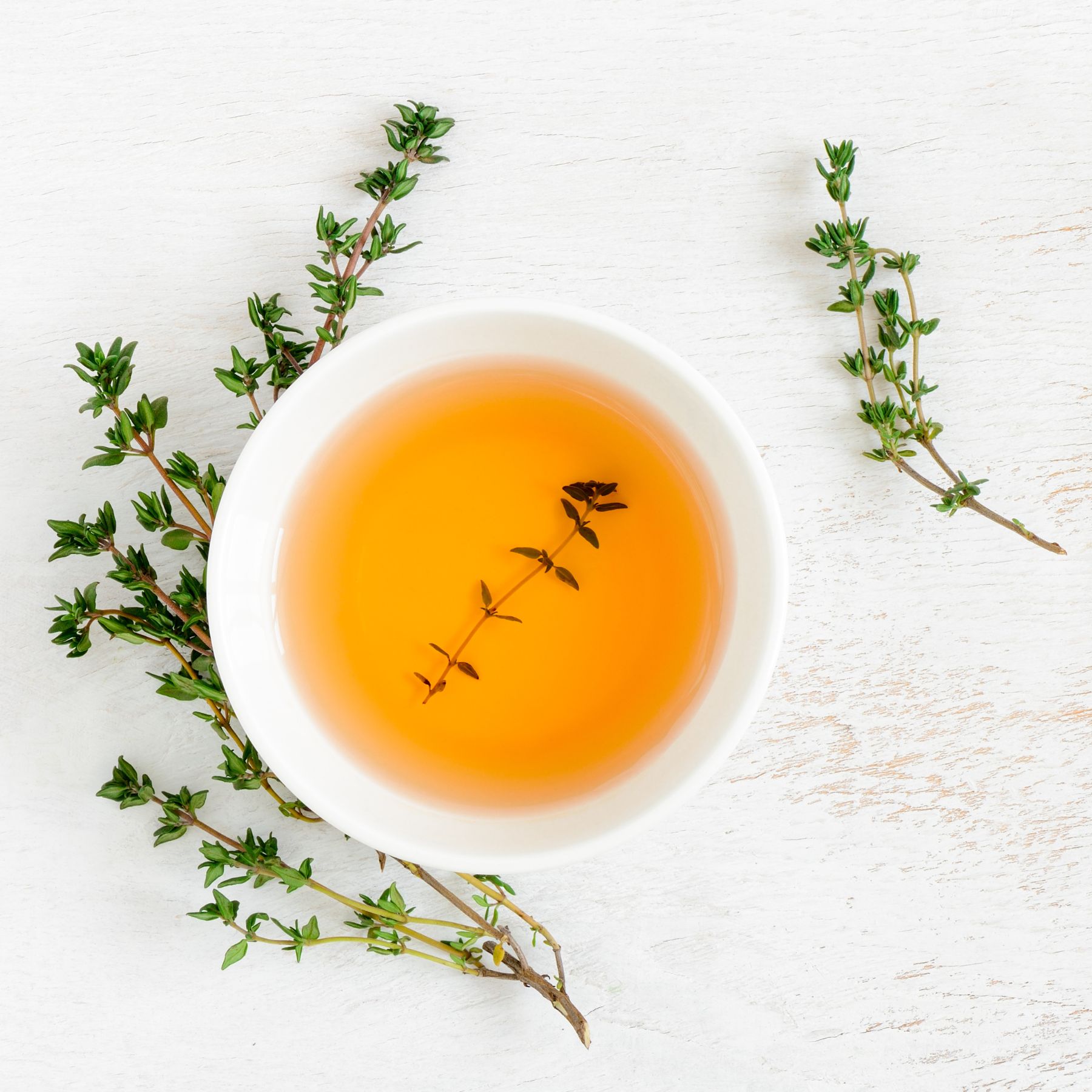 Weiße Schale mit Flüssigkeit, Thymianzweige. Auf hellem Holzgrund. Draufsicht.