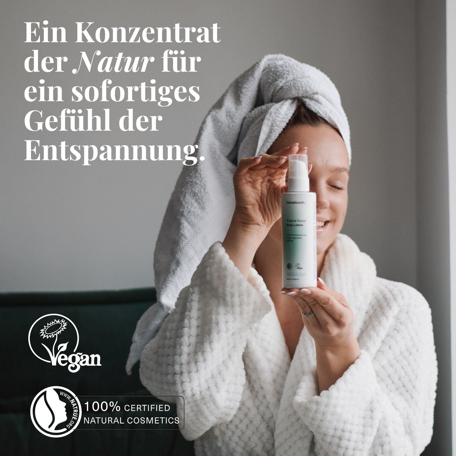 Frau mit Handtuch auf dem Kopf und in einem Bademantel, trägt Lotion auf den Arm auf.