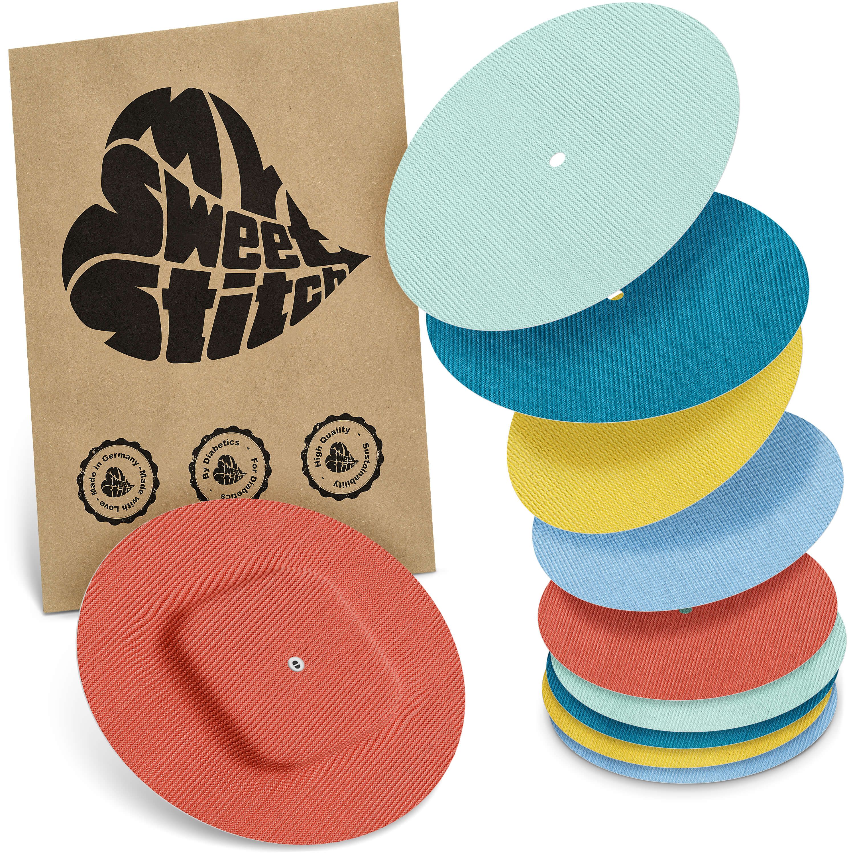 Verschiedenfarbige, runde Pflaster. Eine Packung mit Logo. Mehrere Pflaster sind gestapelt. Rotes Pflaster mit quadratischer Aussparung.