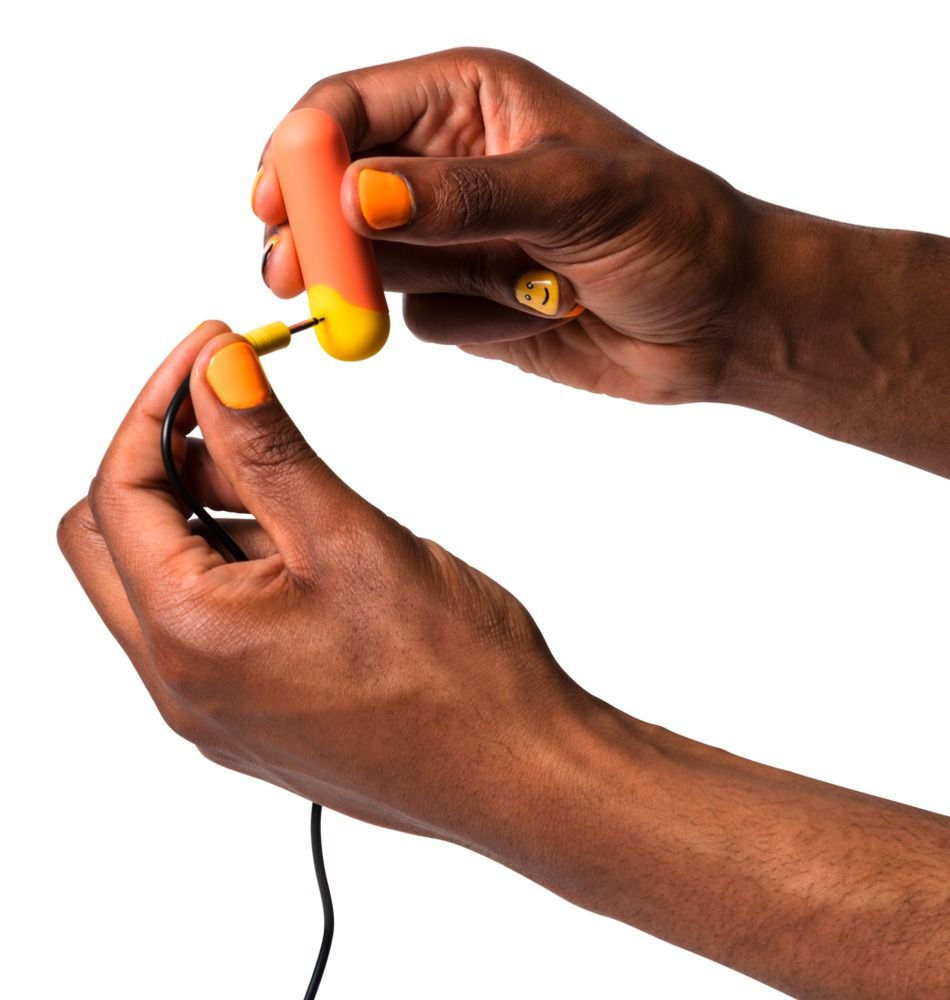 Hände halten orangefarbenen Mini-Vibrator und Ladekabel. Gelbe Nägel.