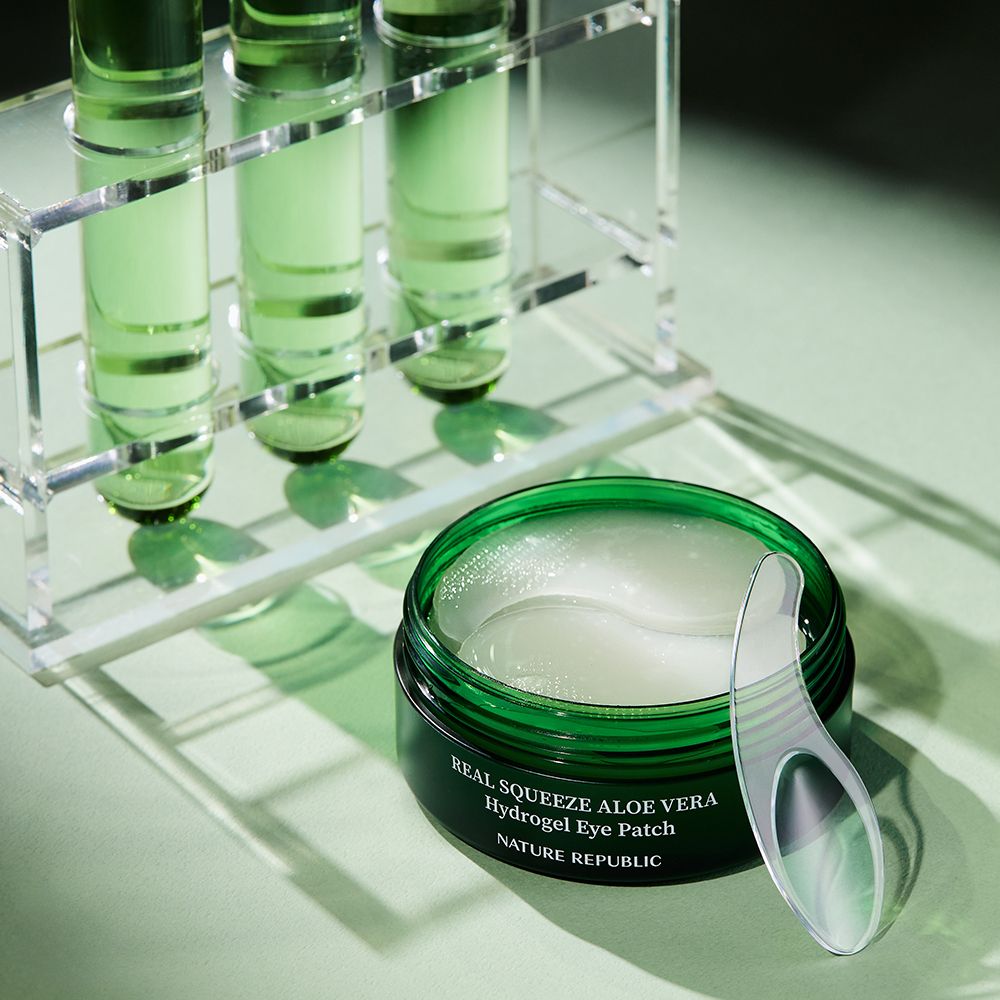 Geöffnete grüne Dose mit Augen-Pads und Spatel. Im Hintergrund Laborutensilien.