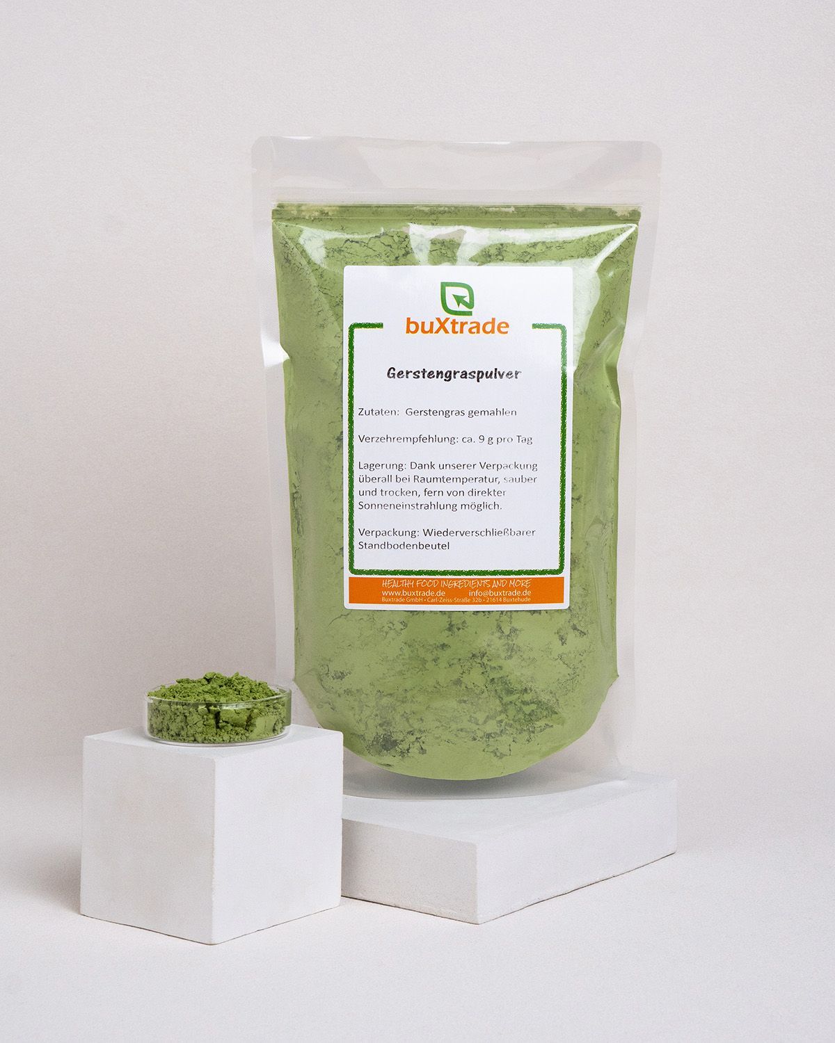 Beutel mit buXtrade Gerstengraspulver. Beutel und Schale mit Pulver auf Podest. Text: Gerstengraspulver, Logo, Inhaltsangaben.