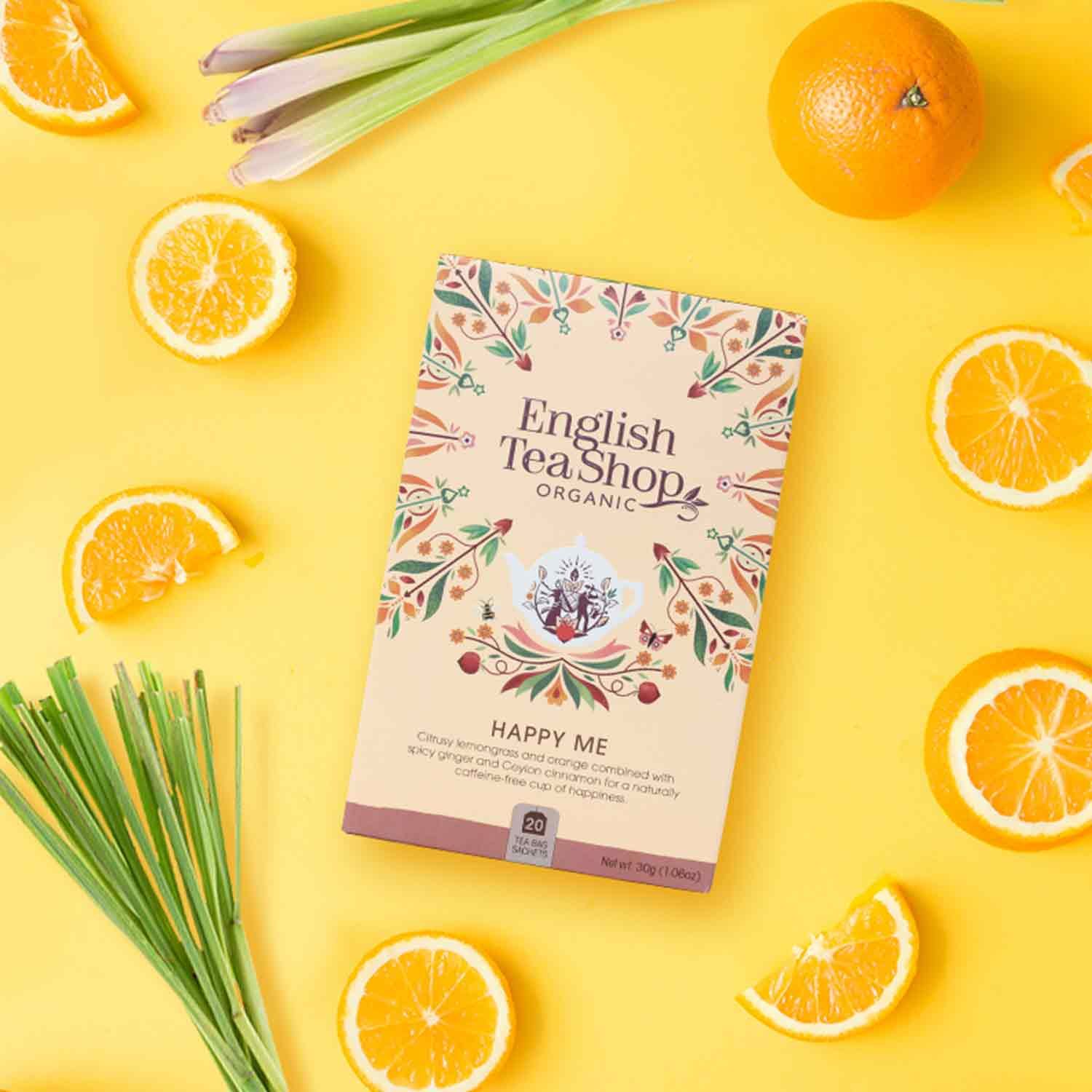 Karton von ETS - Happy Me Wellness-Tee bio. Auf gelbem Hintergrund mit Orangen und Zitronengras. Aufdruck: English Tea Shop Organic, Happy Me.