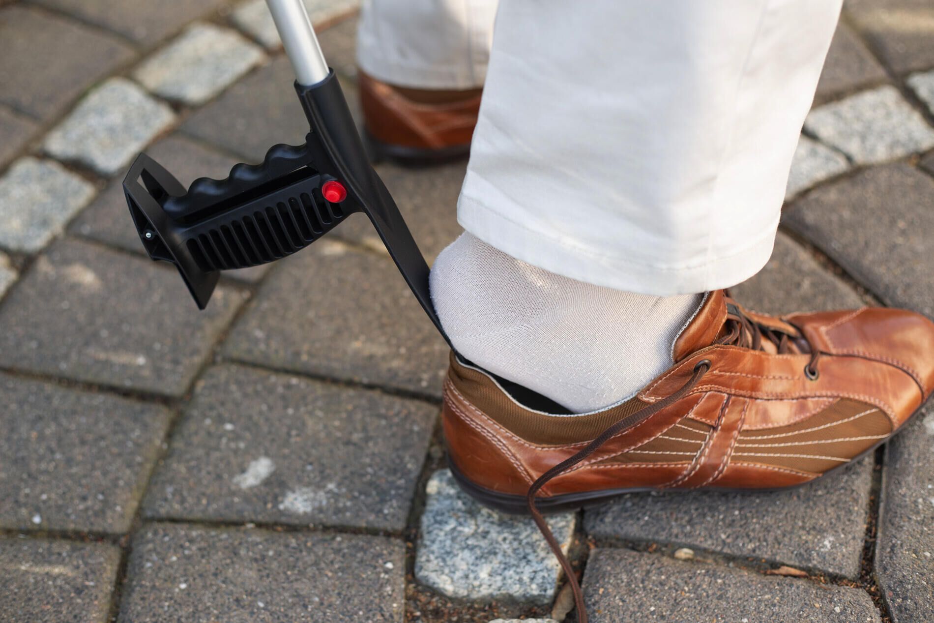 Person benutzt Greifhilfe, um einen Schuh anzuziehen. Schwarzer Griff, roter Knopf.
