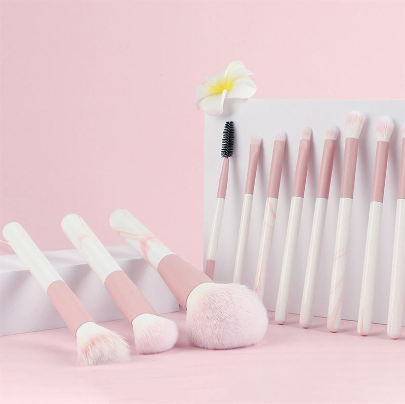 Make-up-Pinsel-Set. Pinsel mit rosa und weißen Griffen. Verschiedene Formen und Größen. Auf rosa Oberfläche platziert. Einige Pinsel sind aufgestellt.