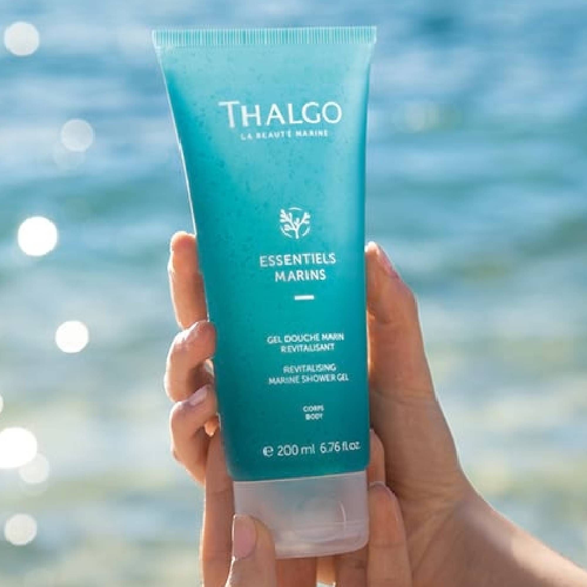 Türkisfarbene Tube, gehalten von einer Hand. Schriftzug: THALGO, ESSENTIELS MARINS, Gel Douche Marin Revitalisant. 200 ml.