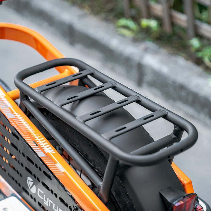 Schwarzer Gepäckträger auf einem orangefarbenen Fahrrad. Rechteckige Form mit Querstreben.