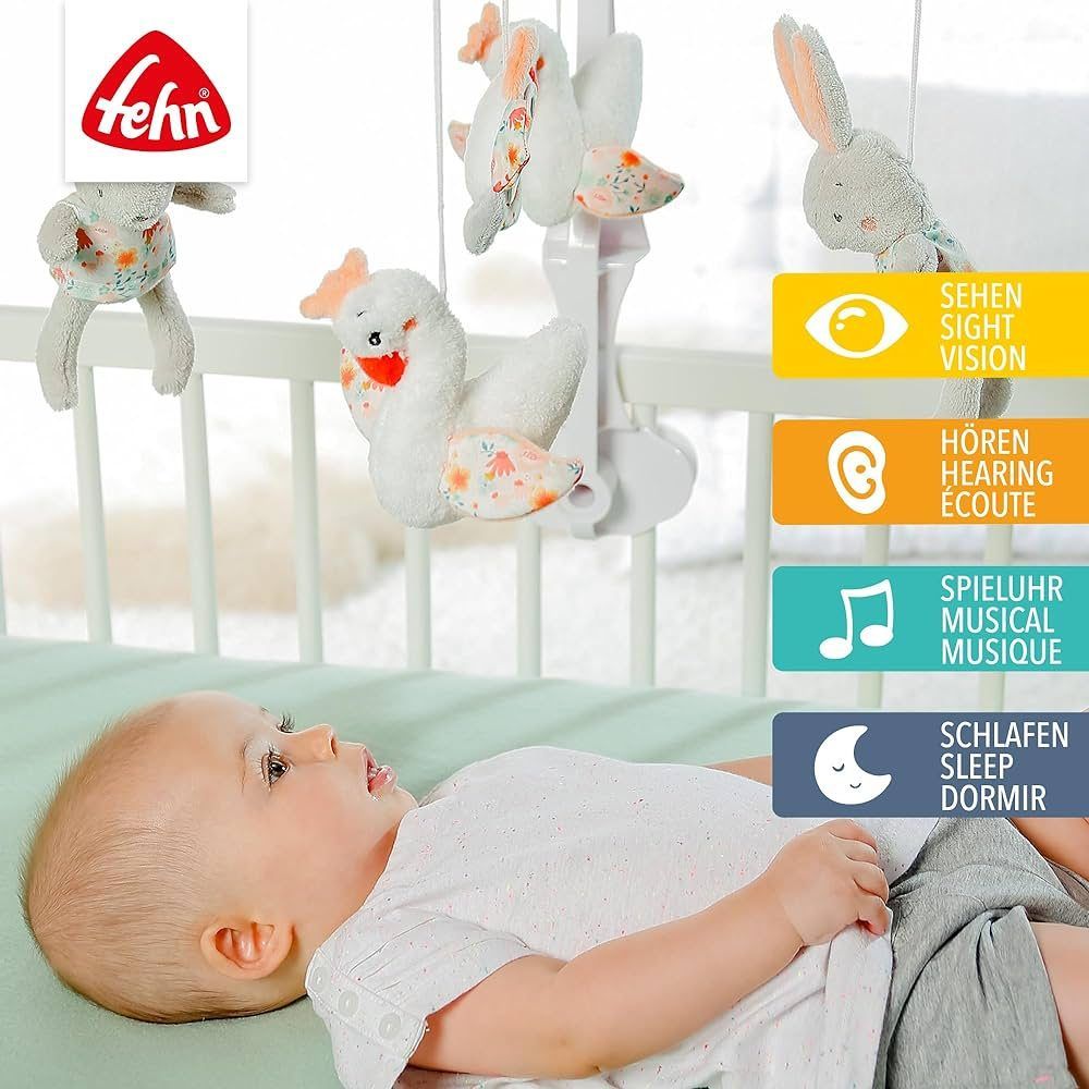 Baby liegt unter Mobile. Mobile mit Hasen, Schwänen und Spiegel. Fehn-Logo. Piktogramme für Sehen, Hören, Spieluhr, Schlaf.