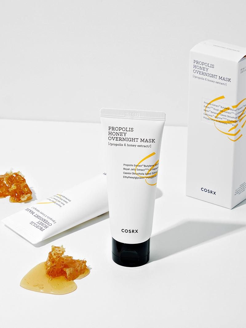 Weiße Tube mit schwarzem Deckel und Karton. Aufschrift: PROPOLIS HONEY OVERNIGHT MASK. Marke: COSRX. Honigwabe und Honig.