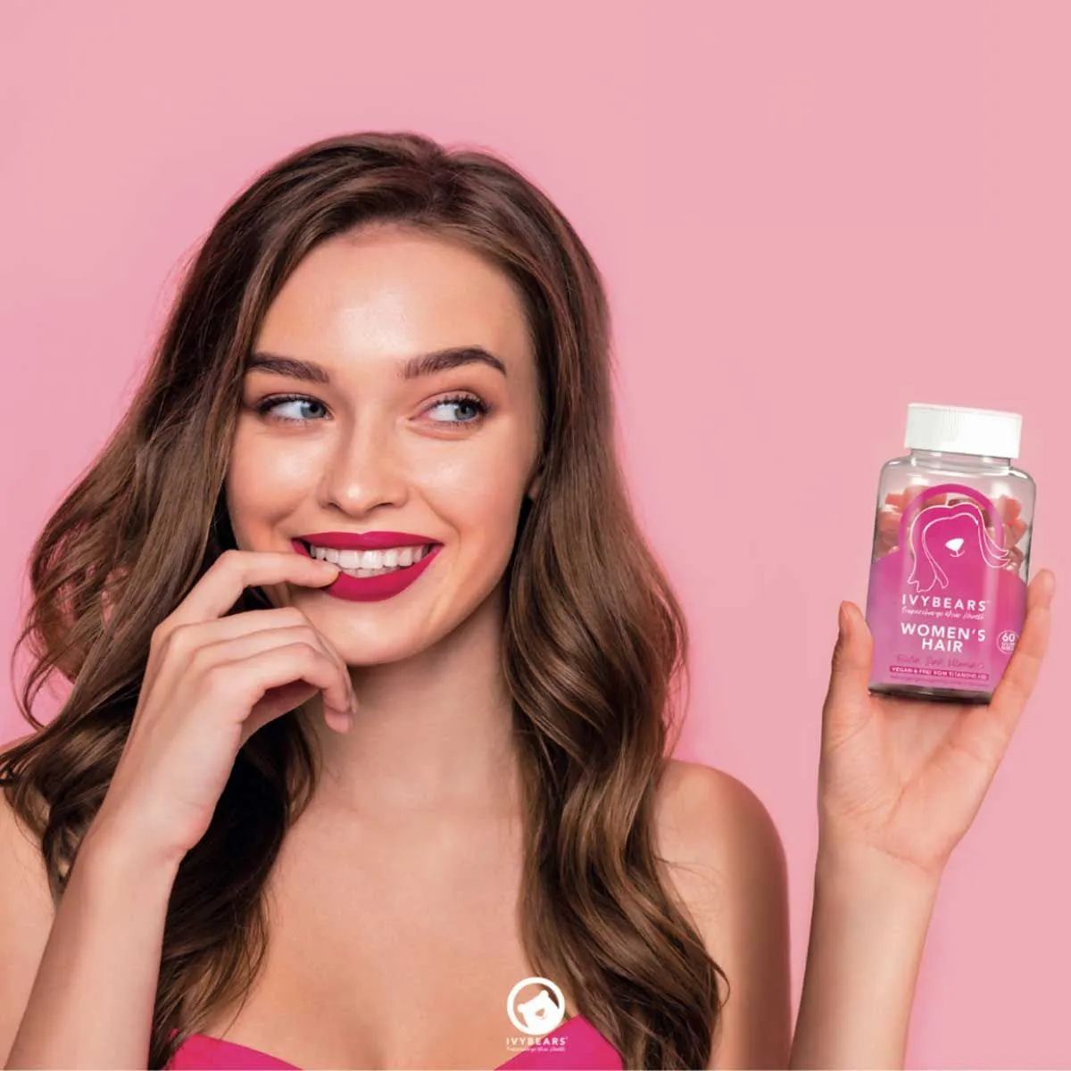 Frau hält eine Flasche mit Gummibärchen. Sie lächelt und berührt ihre Lippen. Rosa Hintergrund.