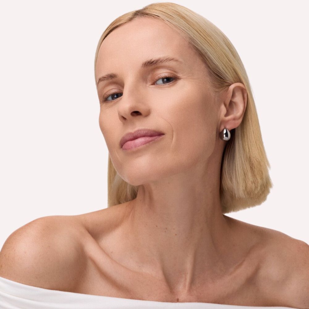 Porträt einer Frau mit blonden Haaren. Sie trägt silberne Ohrringe. Ihr Blick geht nach oben.