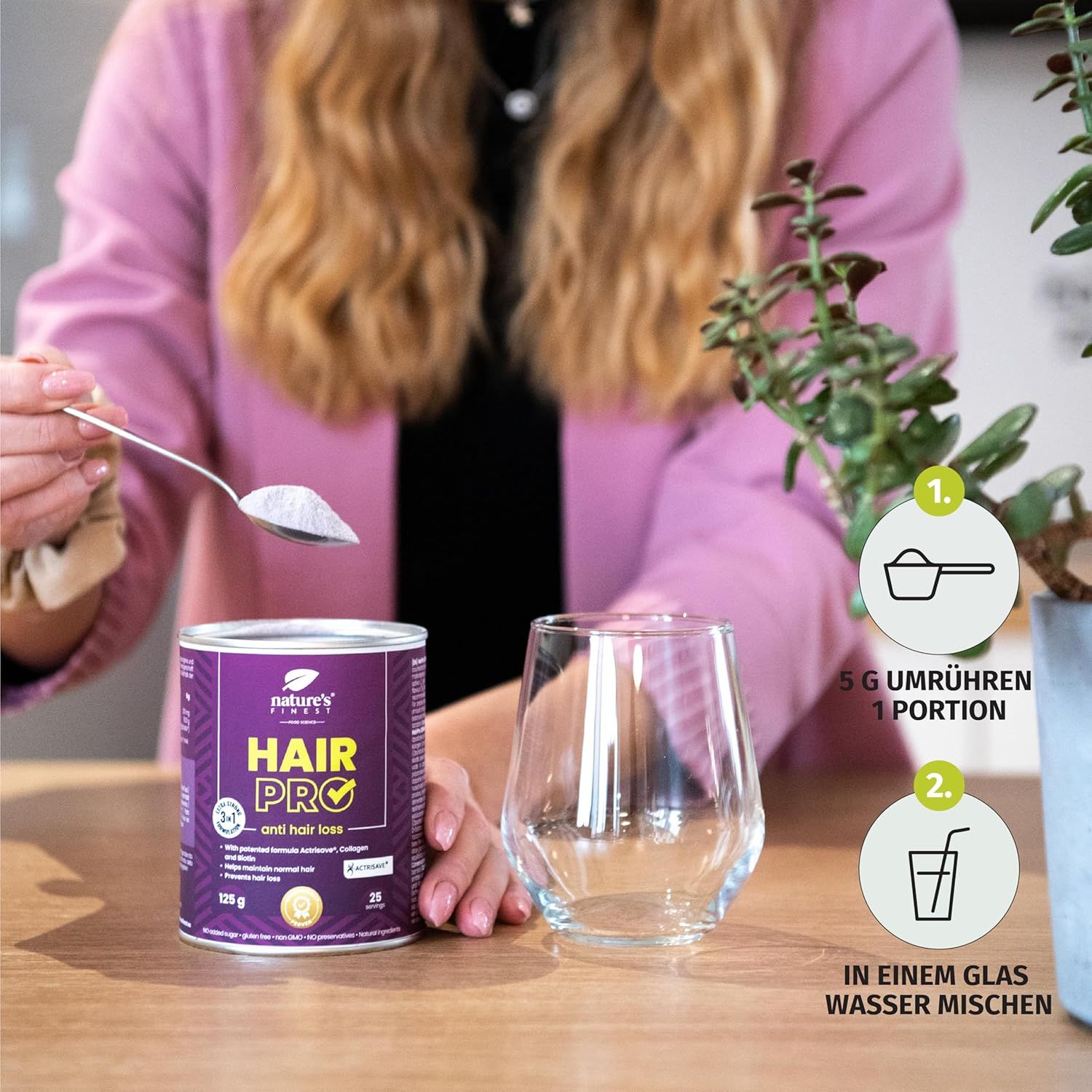 Frau mischt Pulver in Glas. Dose Nature's Finest Hair Pro, Glas. Anweisungen: 5g umrühren, in Wasser mischen.