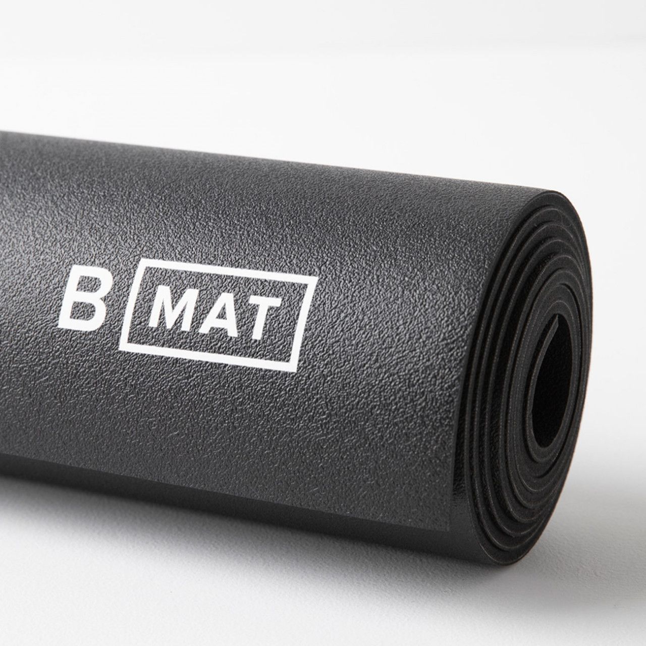 Nahaufnahme einer gerollten schwarzen Yogamatte. Das Logo "B MAT" ist sichtbar.