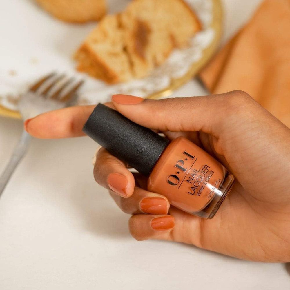 Hand hält OPI Nagellacke Flasche. Lackierte, orangefarbene Nägel. Hintergrund: Essen.