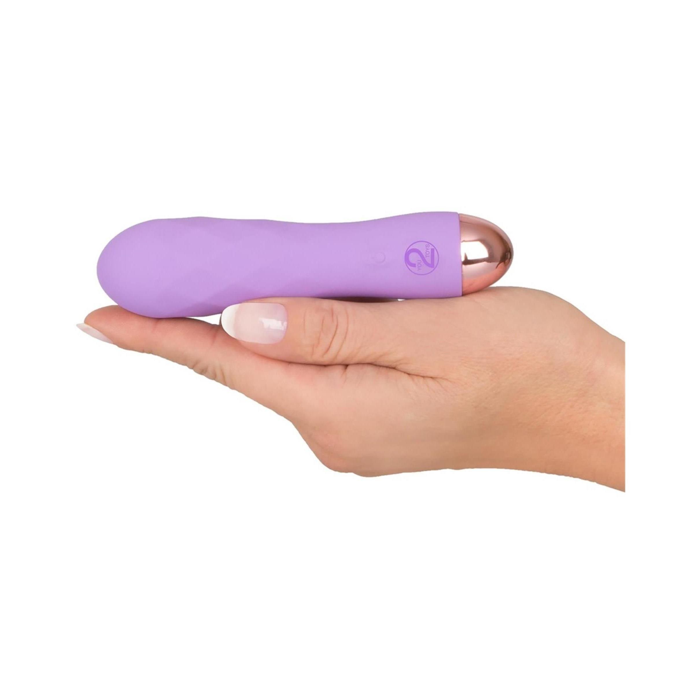 Lila Vibrator in einer Hand gehalten. Goldfarbene Spitze, Bedienknöpfe. Auf weißem Hintergrund.