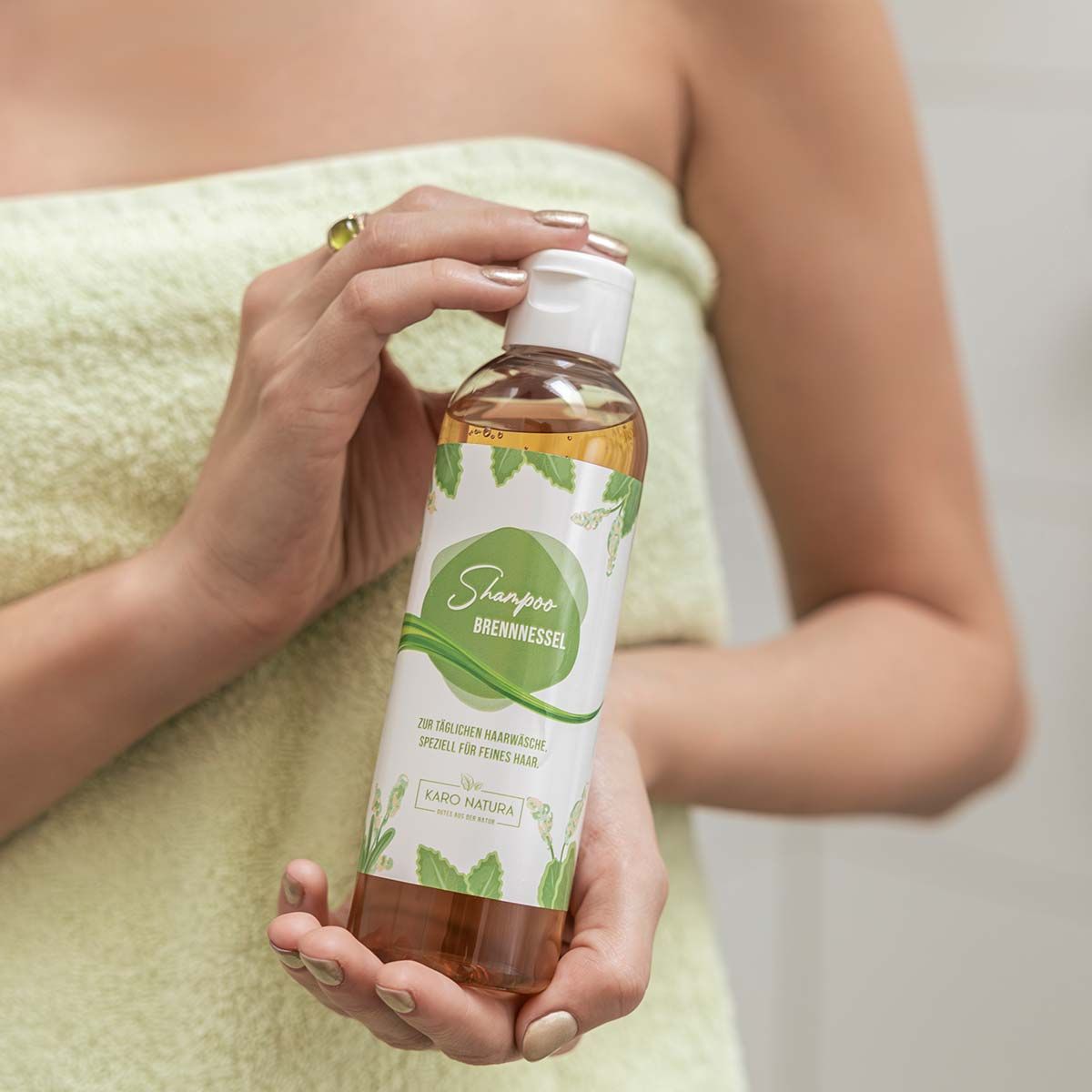 Person hält Shampoo-Flasche. Person in grünem Handtuch. Flasche mit grünem Etikett.