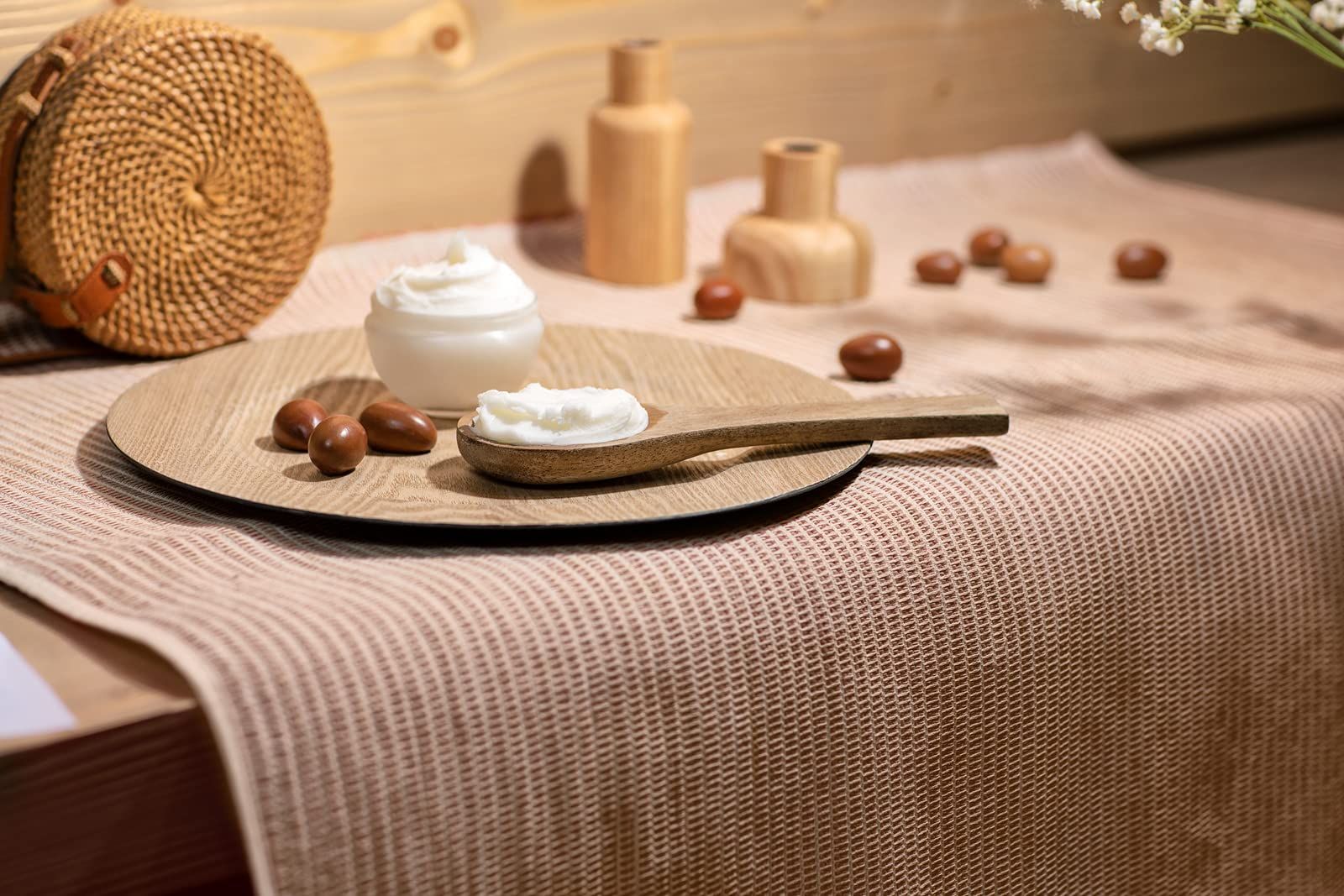 Holztablett mit Creme, Holzschale, Holzschöpfer und Sheabutter-Nüssen. Auf einem Tisch mit Stoff.