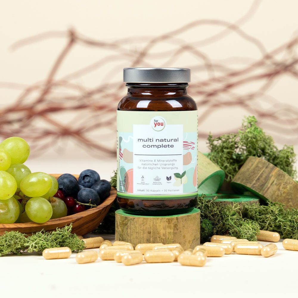 Flasche mit Kapseln auf Holz. Aufschrift: for you multi natural complete. Obst und Moos im Hintergrund.