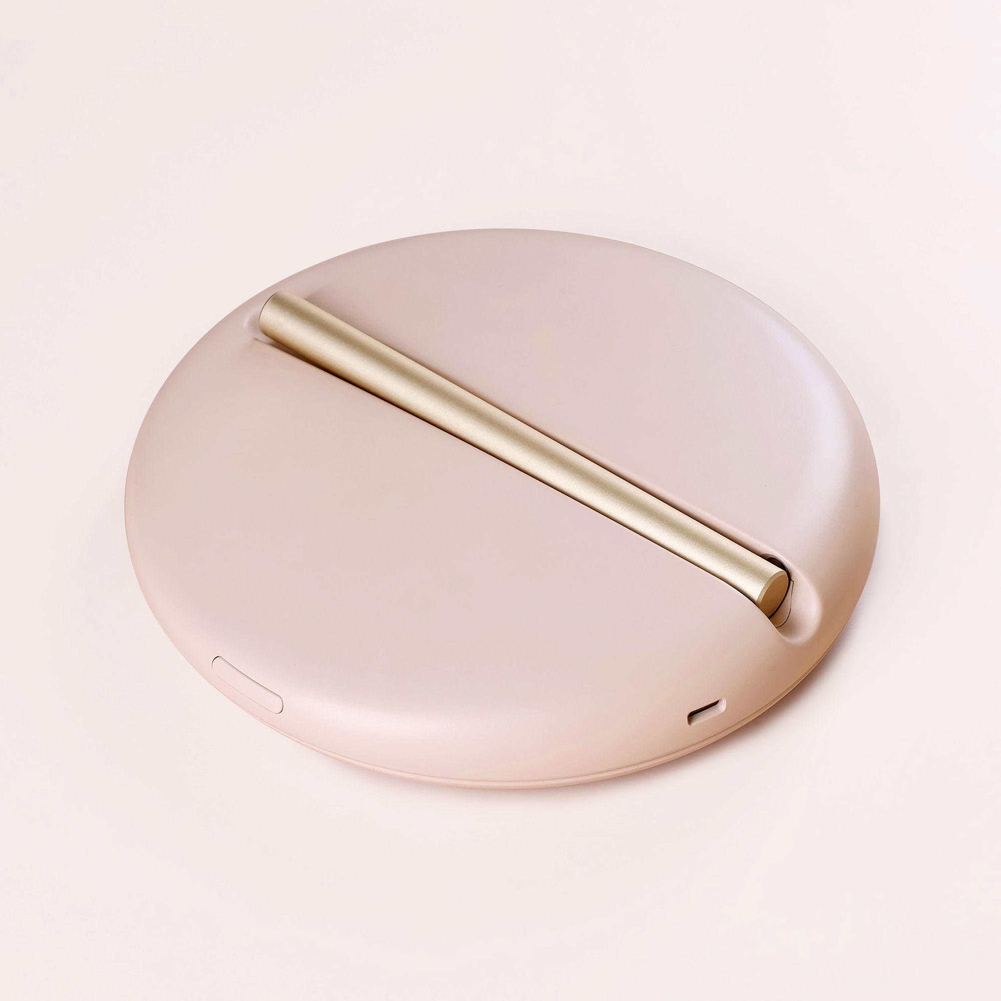 Rosafarbener, runder Spiegel mit goldfarbenem Stiel. Der Stiel dient als Stütze.