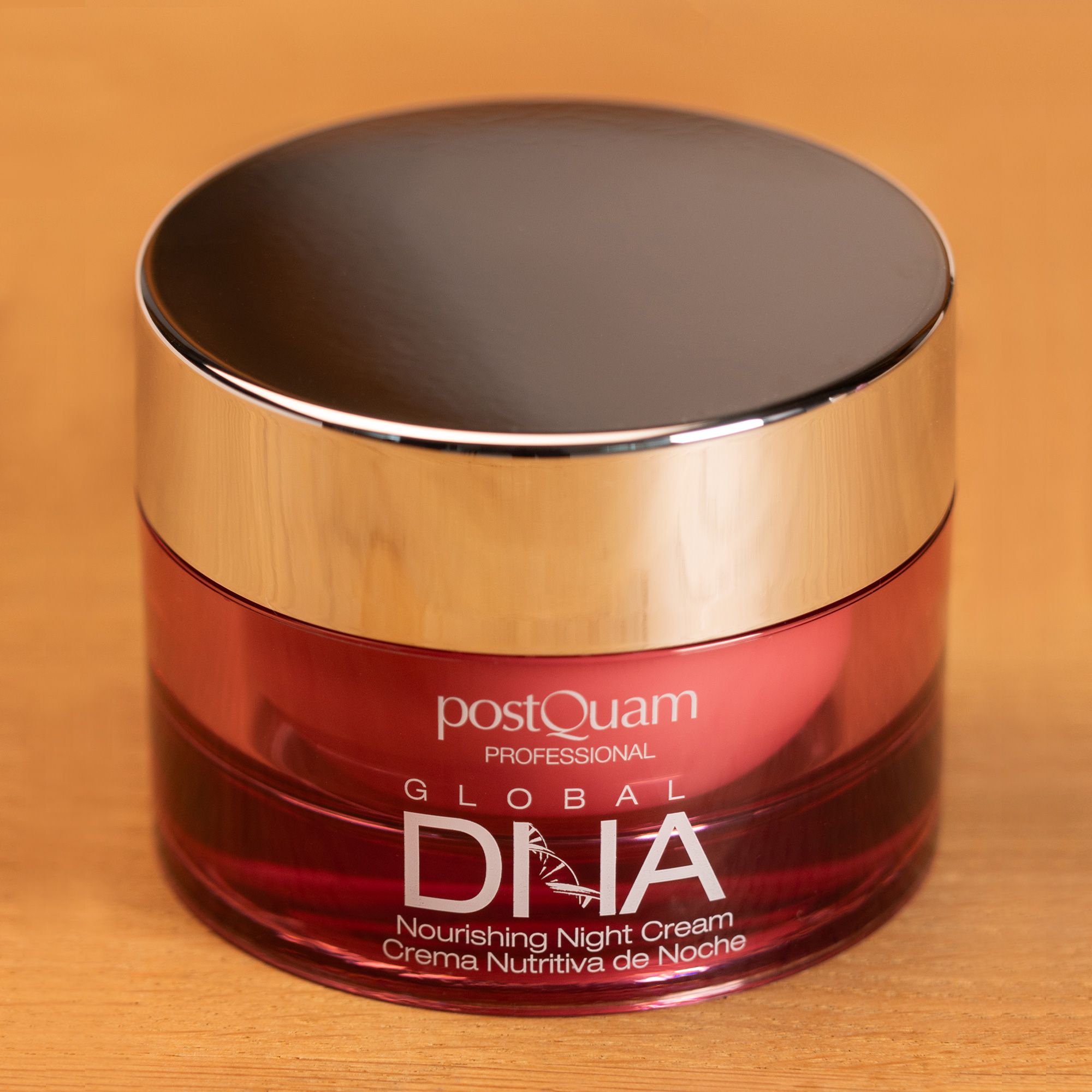Tiegel mit silbernem Deckel. Aufschrift: Postquam Global DNA Nourishing Night Cream. Rosa Creme im Glas, auf Holzuntergrund.