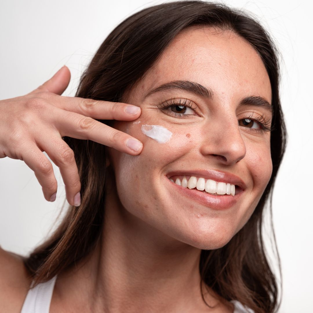 Frau trägt Creme auf ihr Gesicht auf. Weiße Creme auf der Haut. Sie lächelt.