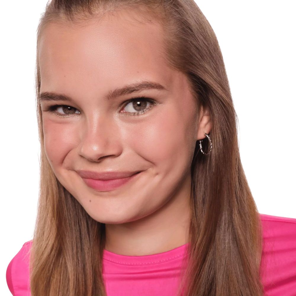 Porträt eines jungen Mädchens mit blonden Haaren und einem rosa Oberteil. Sie trägt Ohrringe.