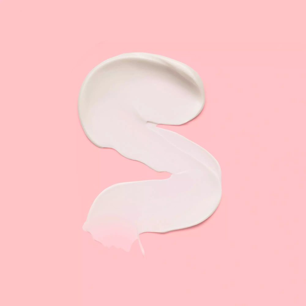 Creme-Produkt-Abstrich in S-Form auf rosa Hintergrund. Keine Marke oder Text sichtbar.