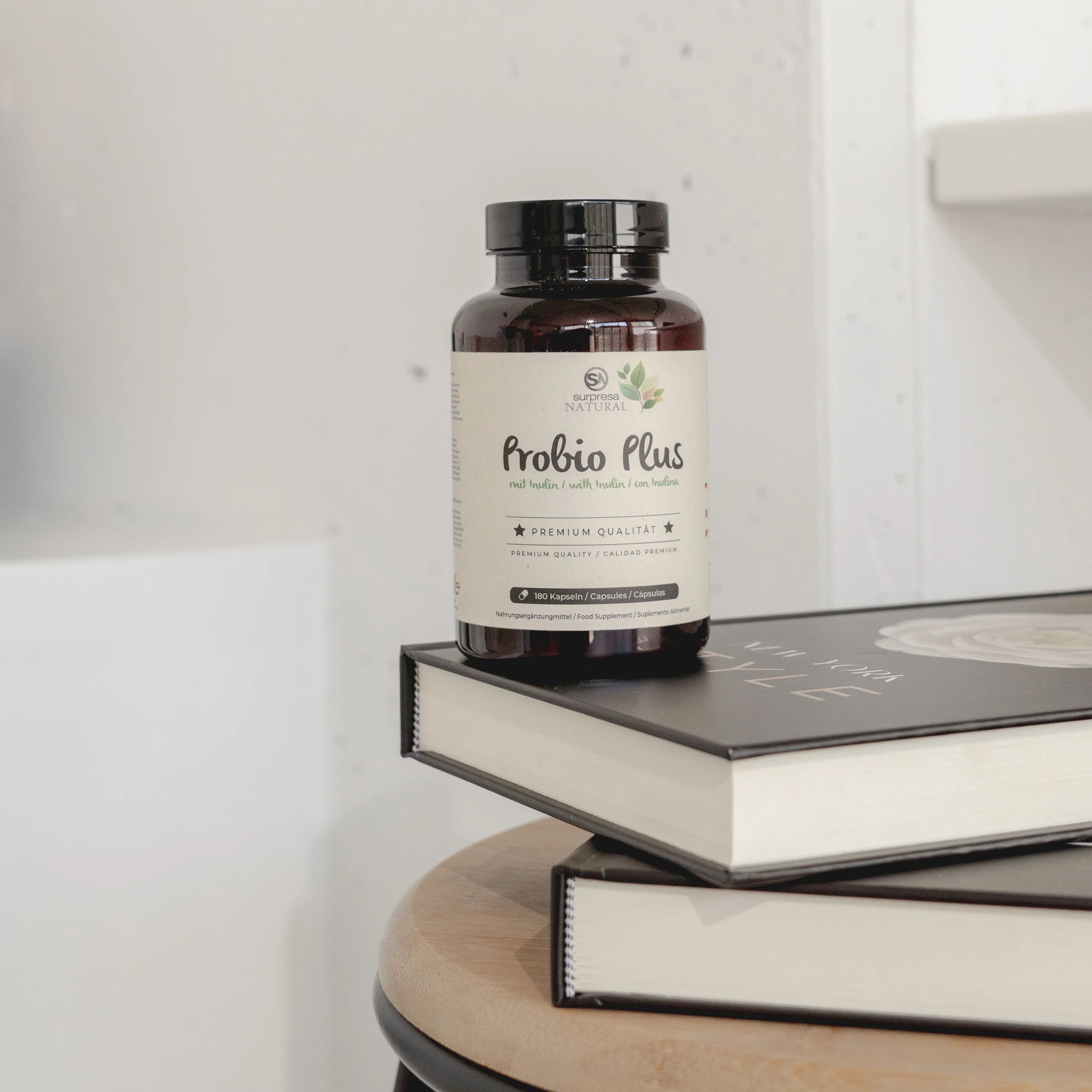 Produktflasche auf Büchern. Aufschrift: Surpresa Natural Probio Plus. Braune Flasche mit schwarzem Deckel.