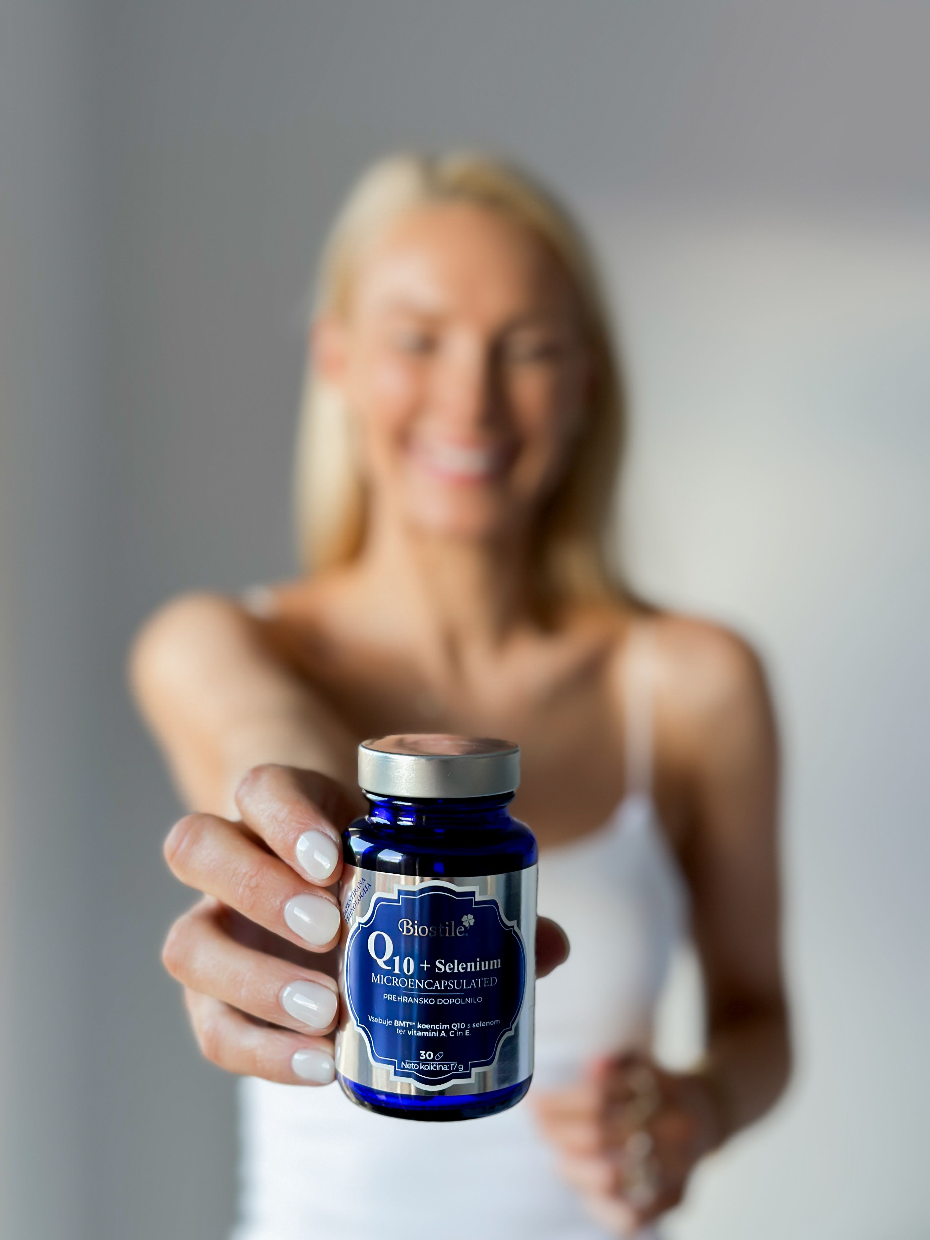 Frau hält blaue Flasche mit Produktetikett. Aufschrift: Q10+Selenium Microencapsulated. 30 Kapseln.