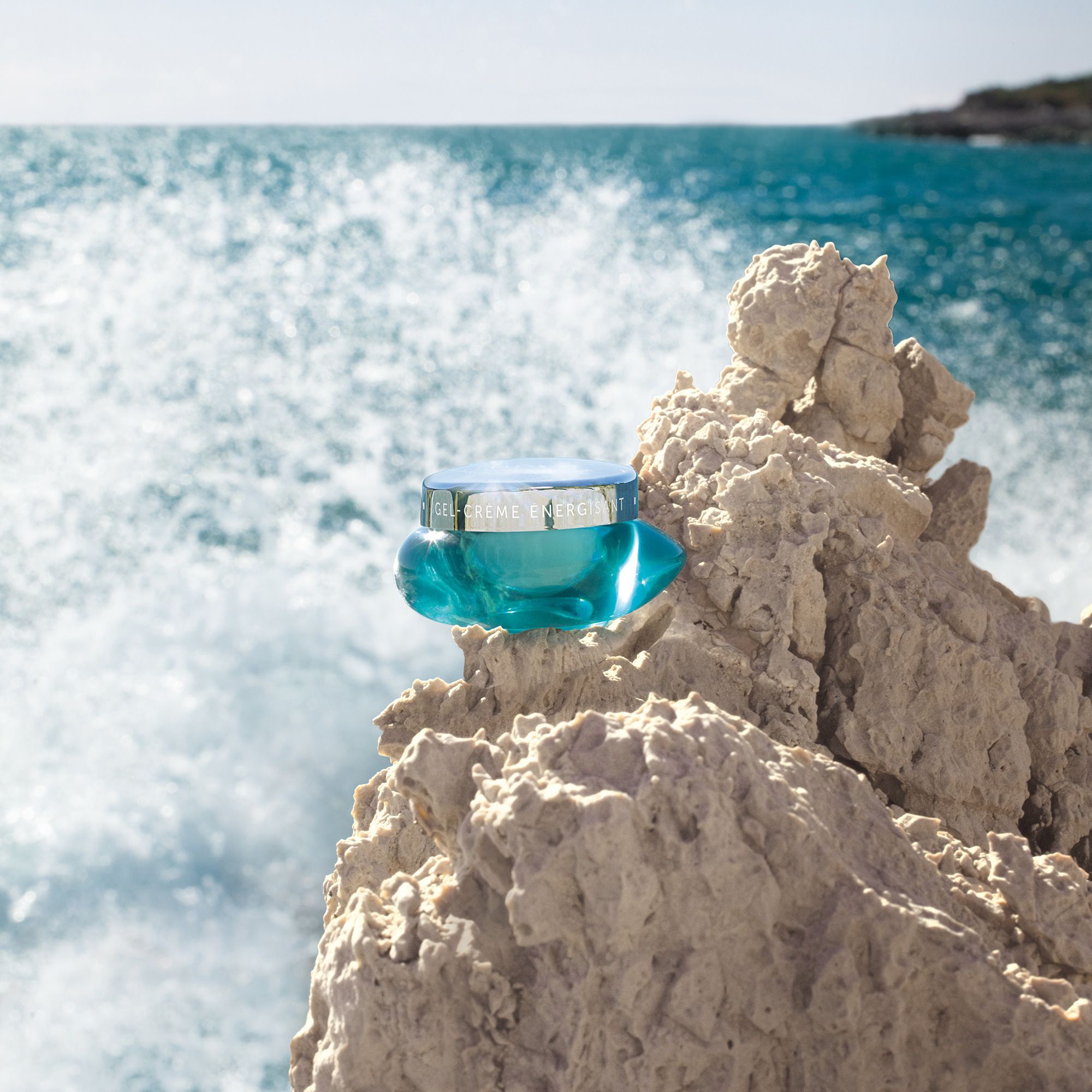 Türkisfarbener Tiegel auf Felsen vor Meer. Silberner Deckel, Aufschrift: GEL-CRÈME ÉNERGISANT. Marke THALGO.