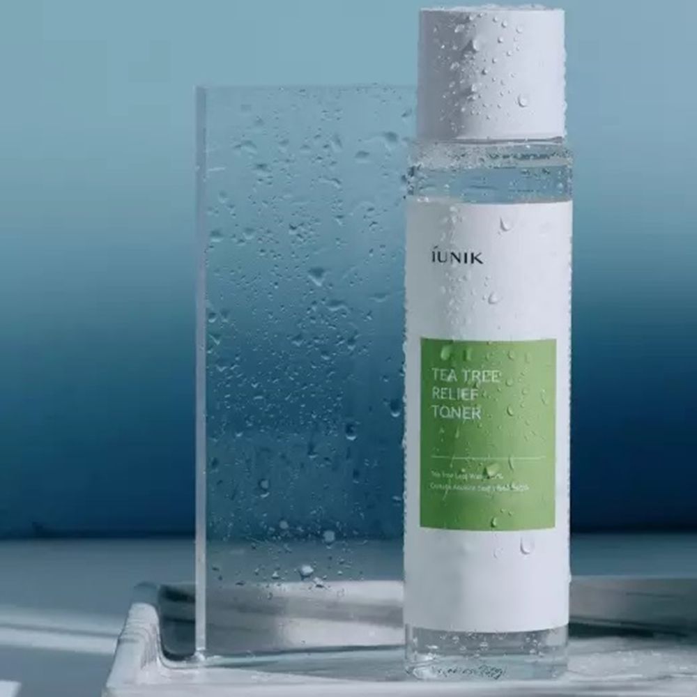 Transparente Flasche mit weißem Deckel, bedeckt mit Wassertropfen. Grün-weißes Etikett mit Text: IUNIK, Tea Tree Relief Toner.