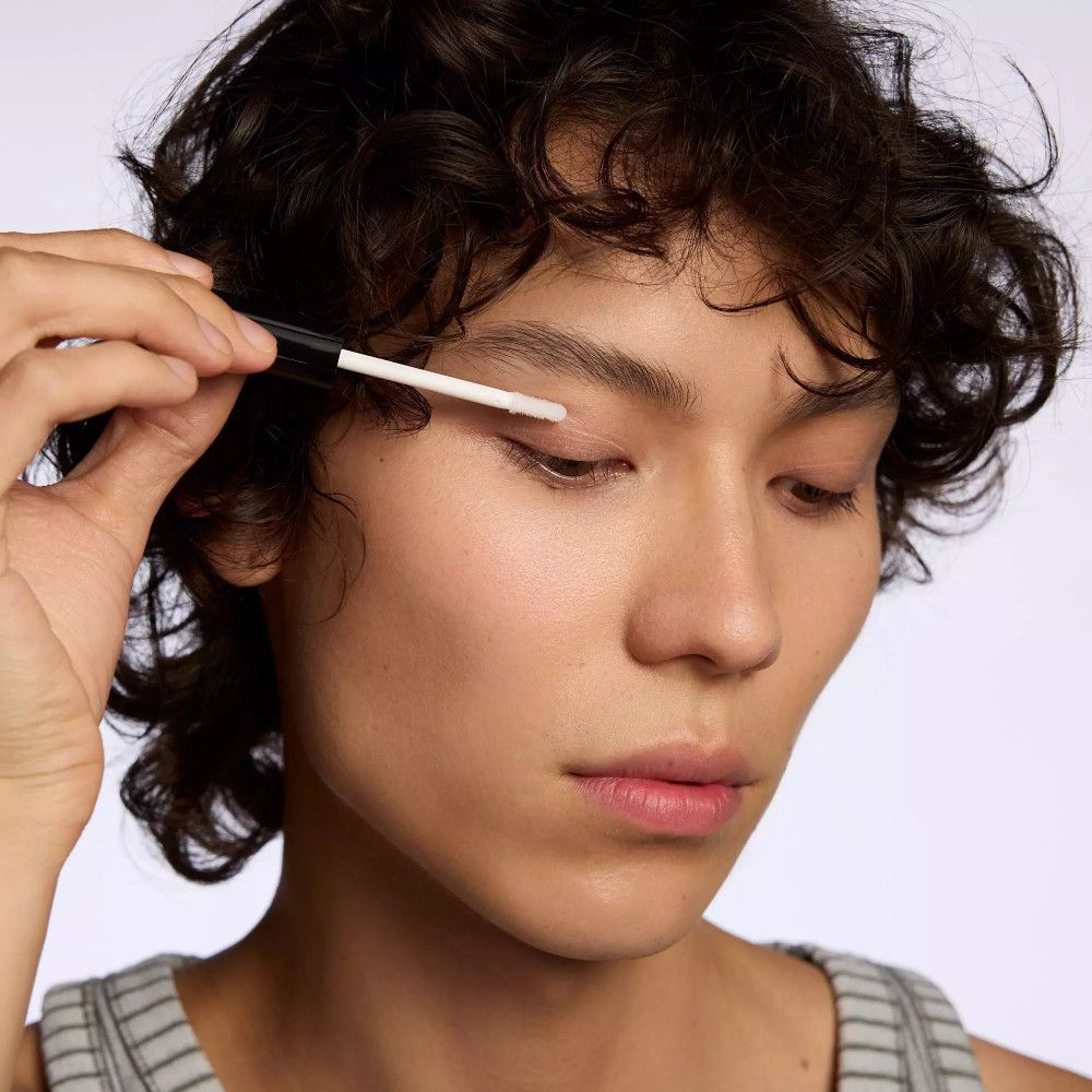 Person hält Applikator an Augenlid. Hautton, helle Haut. Anwendung des Produkts.