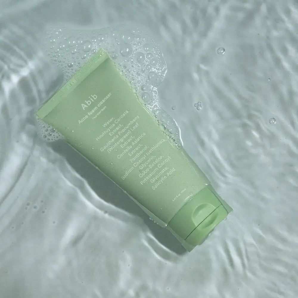 Hellgrüne Tube mit Produktnamen und Inhaltsstoffen. Liegt in Wasser mit Blasen.