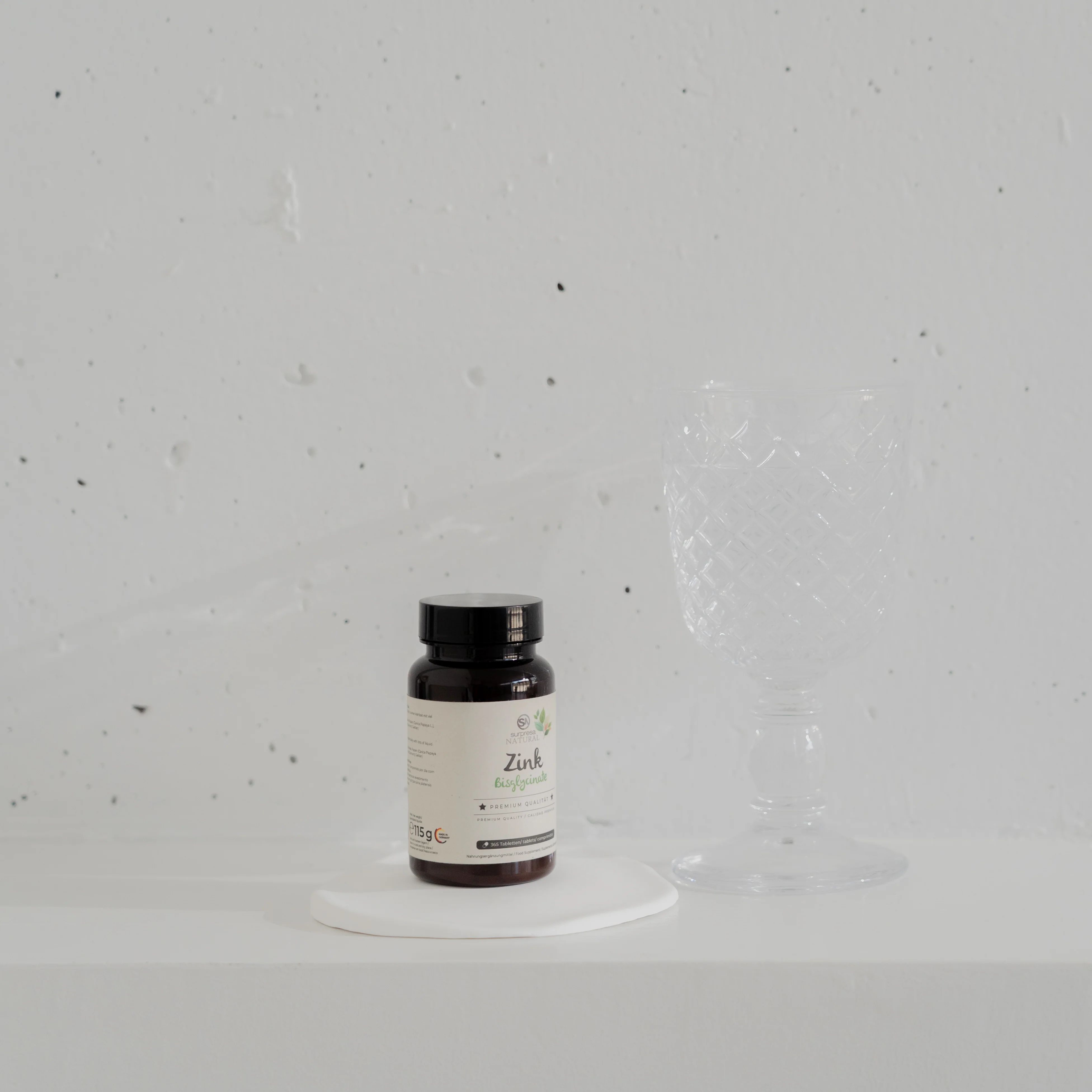 Braune Flasche mit Etikett steht auf weißer Unterlage. Daneben ein Glas. Hintergrund weiß.