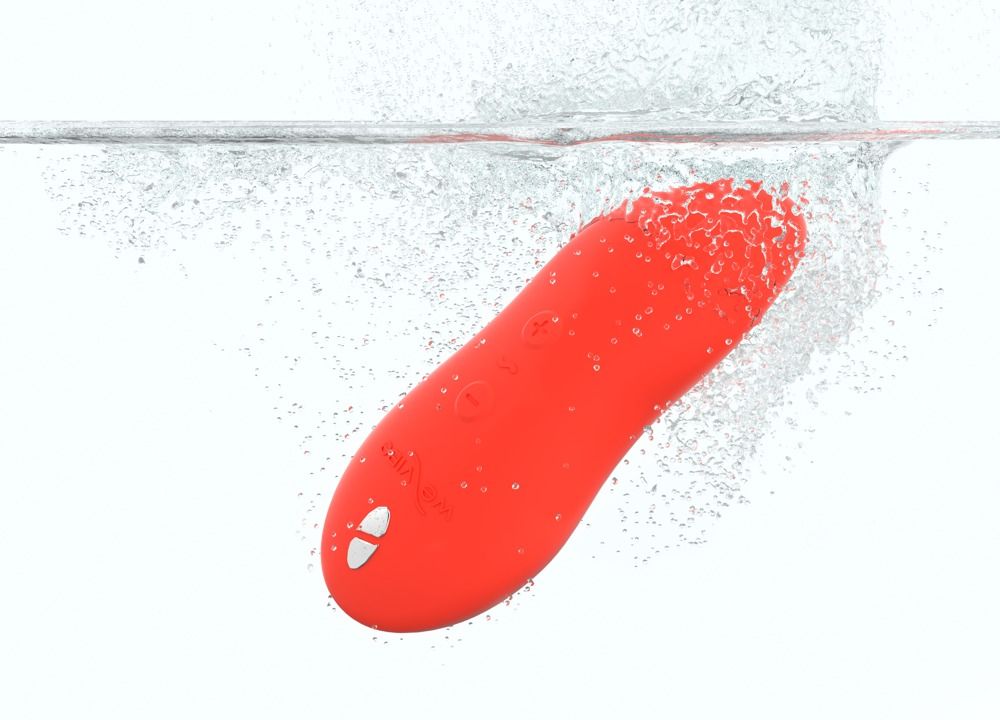 Korallenfarbenes, längliches Gerät im Wasser. Ein Ende mit einer Taste. Wasser spritzt.