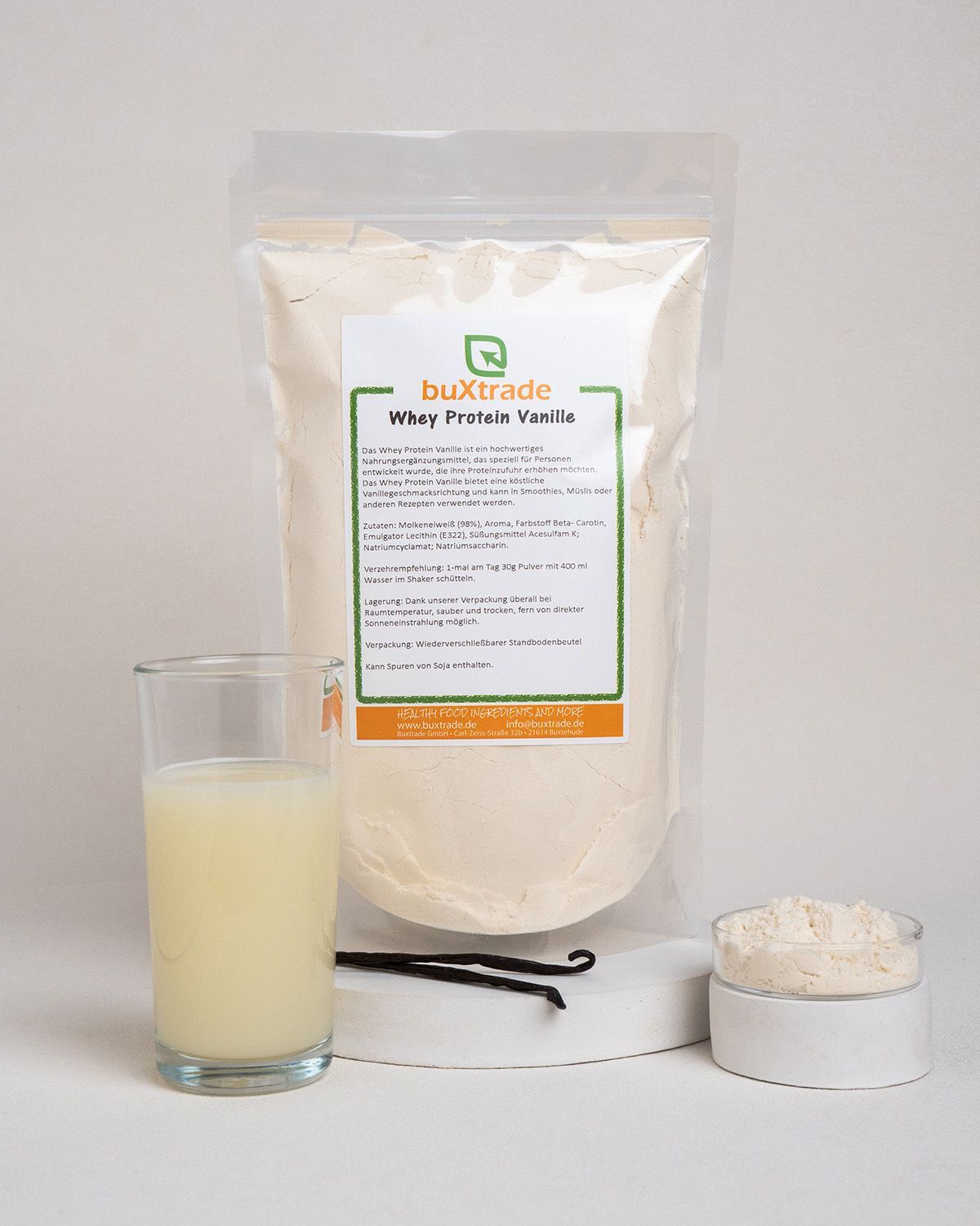 Beutel, Glas mit Flüssigkeit, Löffel mit Pulver, Vanilleschoten. buXtrade Whey Protein Vanille. Text auf Deutsch.