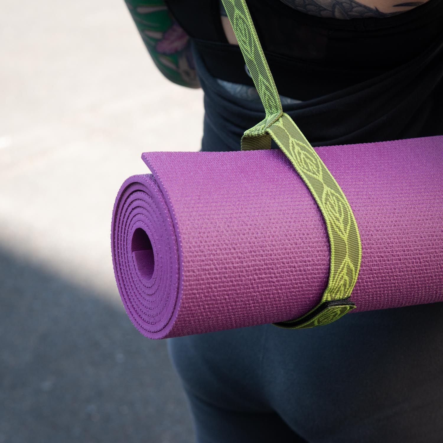 Gerollte Yogamatte, pink, mit grünem Tragegurt. Gurt mit Muster. Nahaufnahme.