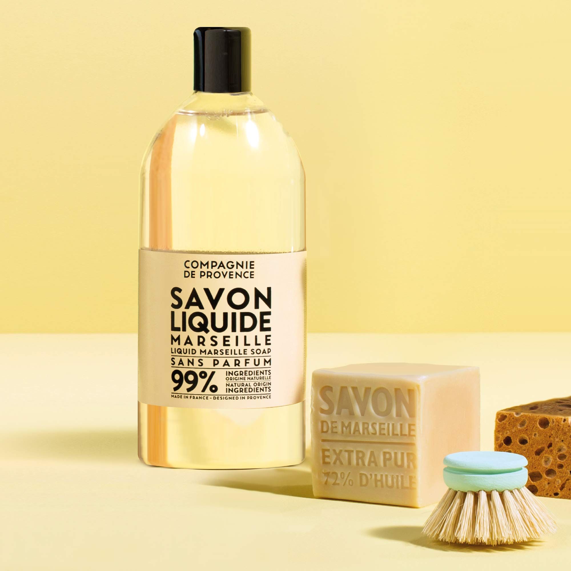 Transparente Flasche mit schwarzem Deckel, daneben Seifenstück, Bürste und Schwamm. Aufschrift: Savon Liquide Marseille.
