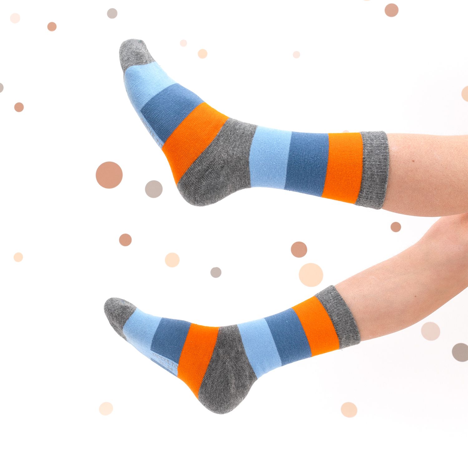 Zwei Füße mit gestreiften Socken in Blau, Grau und Orange, getragen mit grauen Socken. Hintergrund mit braunen Punkten.