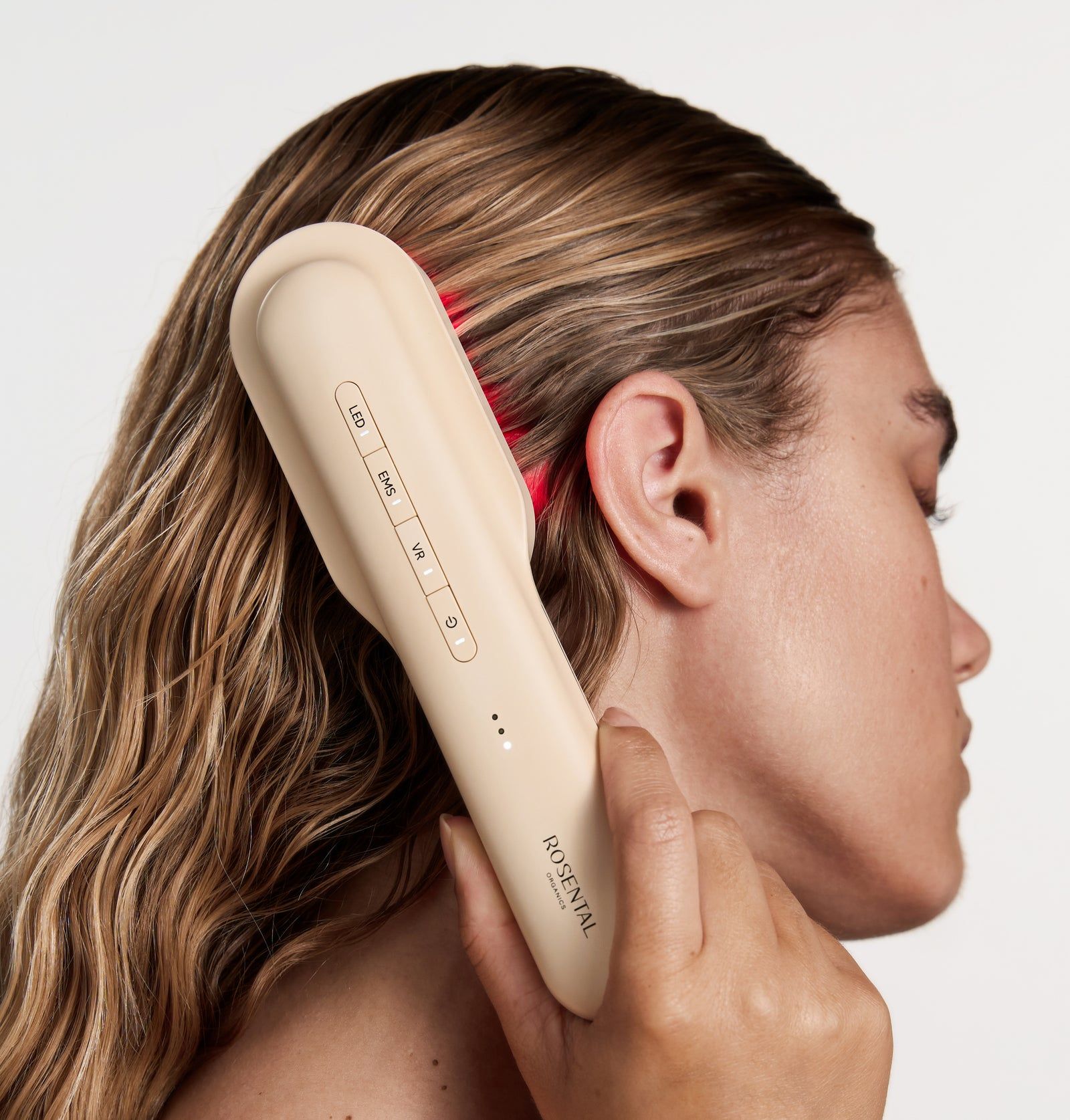 Person hält beigefarbene LED-Haarbürste am Haaransatz. Rotes Licht sichtbar. Rosental-Logo.