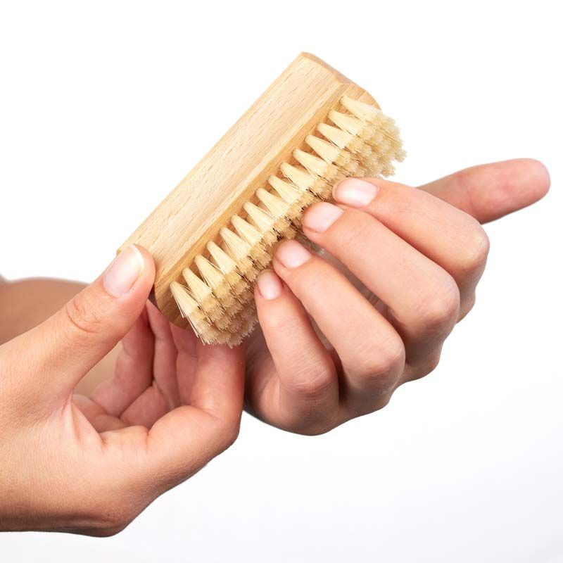 Hand hält Hand- und Nagelbürste aus Holz mit Naturborsten. Bürste wird zwischen den Fingern gehalten, Nahaufnahme.