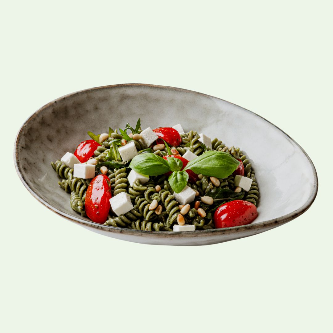 Schüssel mit Spirulix-Nudeln, Tomaten, Käse, Pinienkernen und Basilikum. Gericht in einer ovalen Schale.