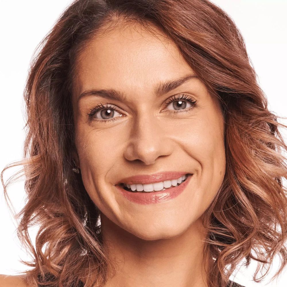 Porträt einer lächelnden Frau. Sie hat braunes Haar und trägt Make-up.