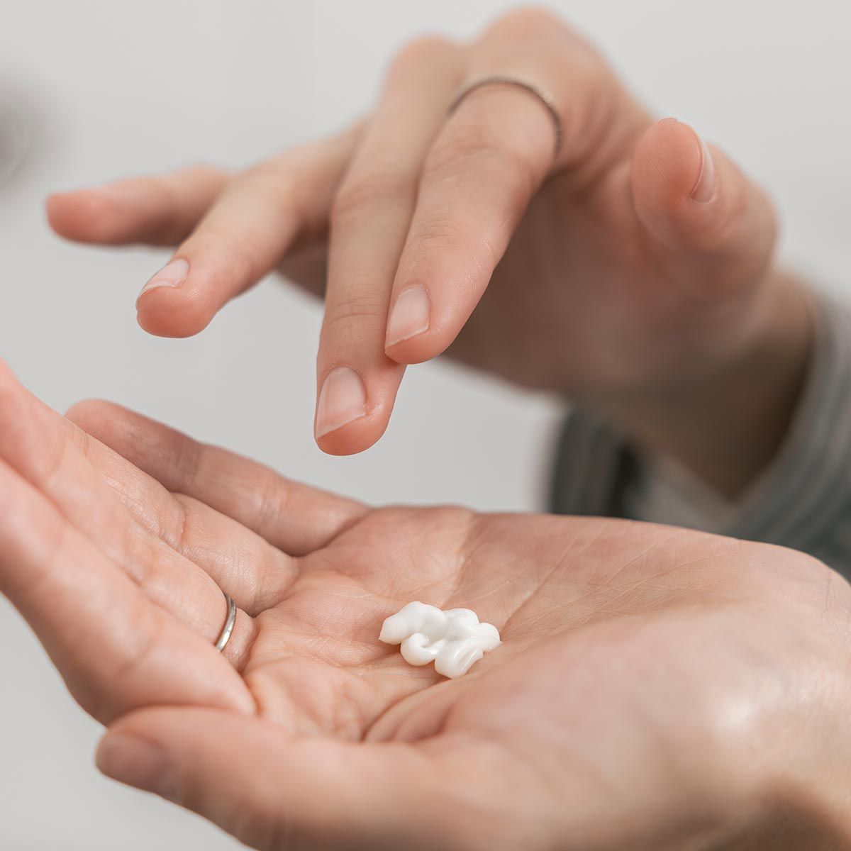 Hände mit einer kleinen Menge weißer Creme. Ringe an den Fingern.