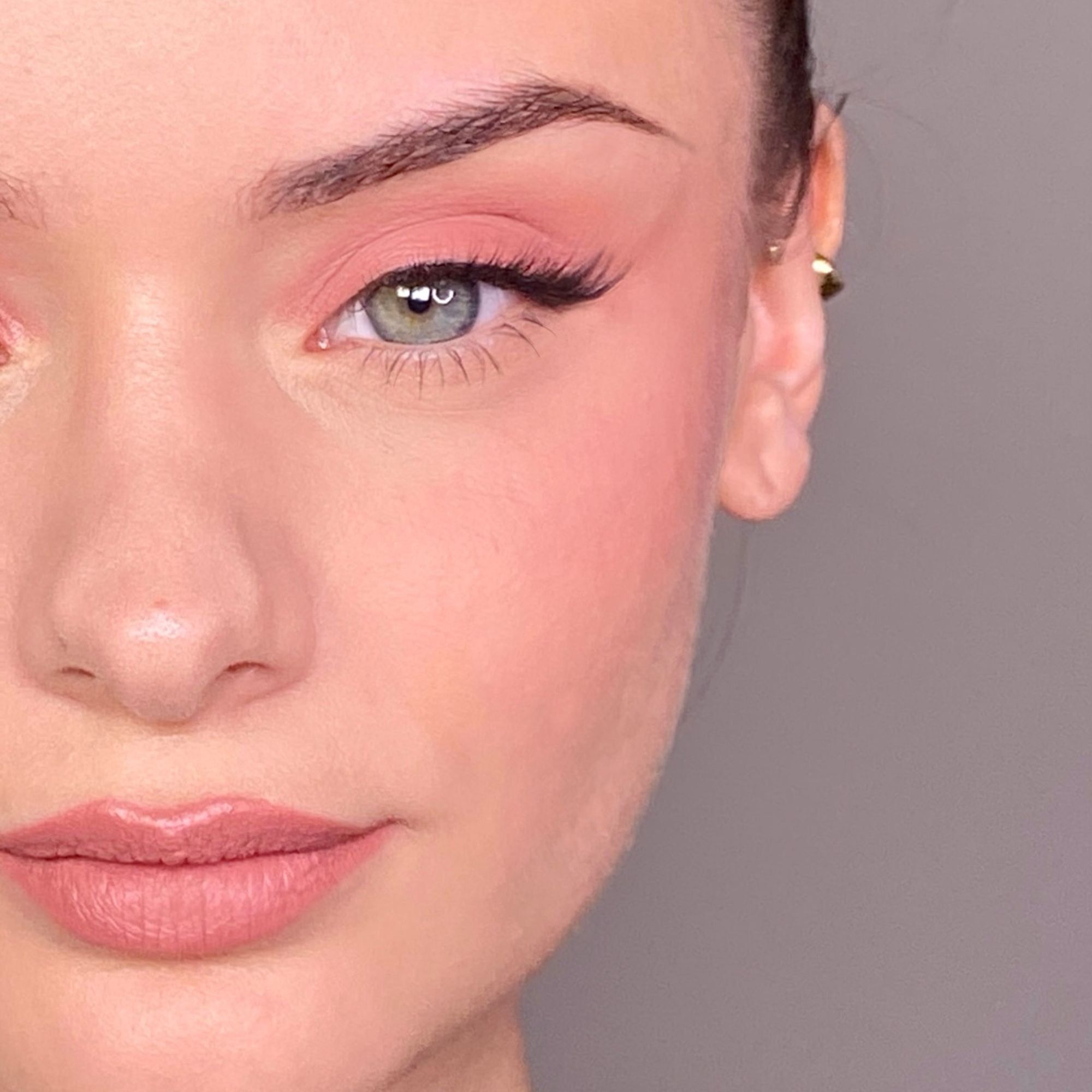 Nahaufnahme eines Gesichts mit Make-up. Augen, Lippen und Wangen sind rosa geschminkt.