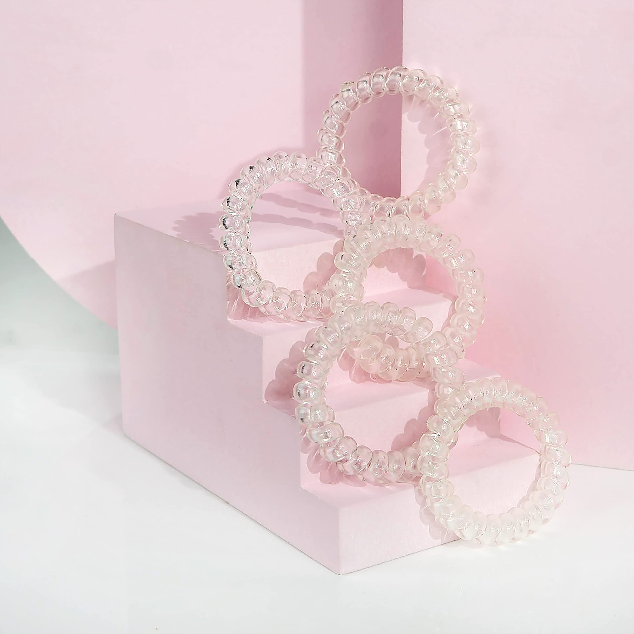 Mehrere transparente Haargummis in Spiralform auf rosa Stufen angeordnet.